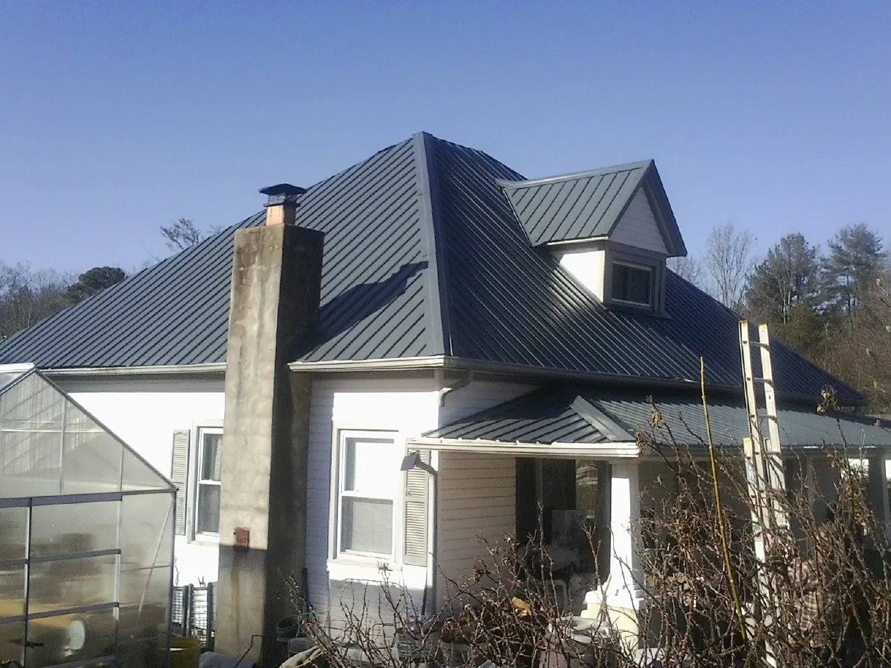 Dark blue standing seam metal roof on a white farmhouse with dormer — Slate & Tile Roof Repair by Roofing Brothers in Fort Rock