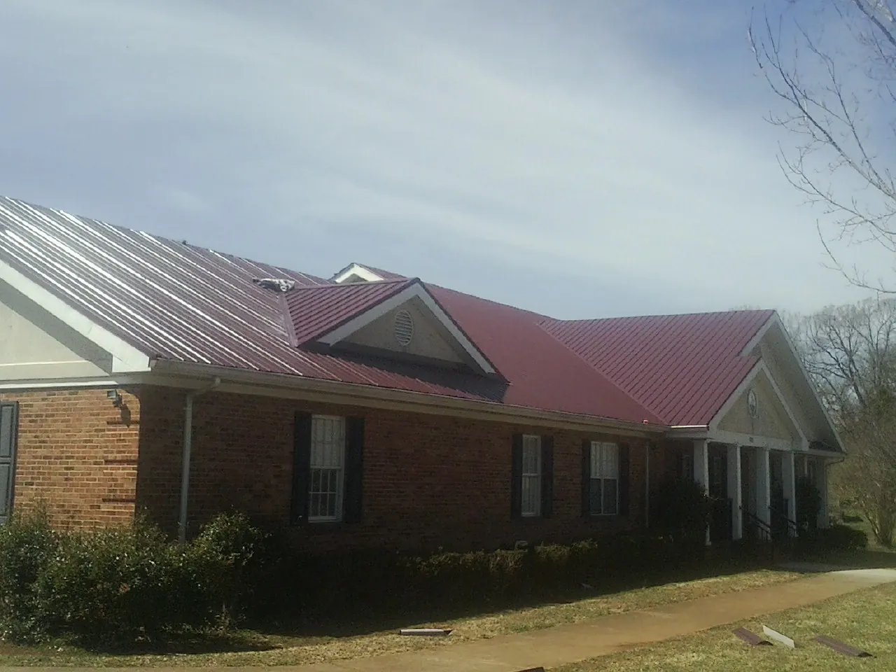 Red metal roof with gabled entries on a long brick building, from a Hail Damage Roof Repair job in Fort Rock