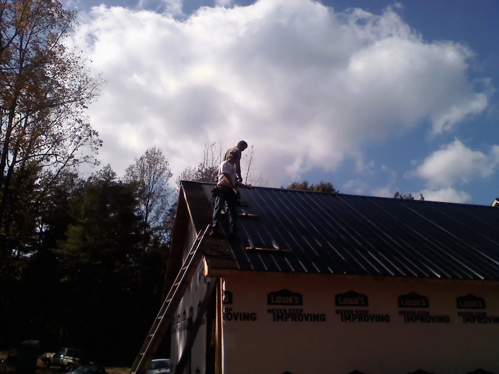 Roofer fastening dark metal panels high against a cloudy sky, from a Roof Inspection job in Fort Rock