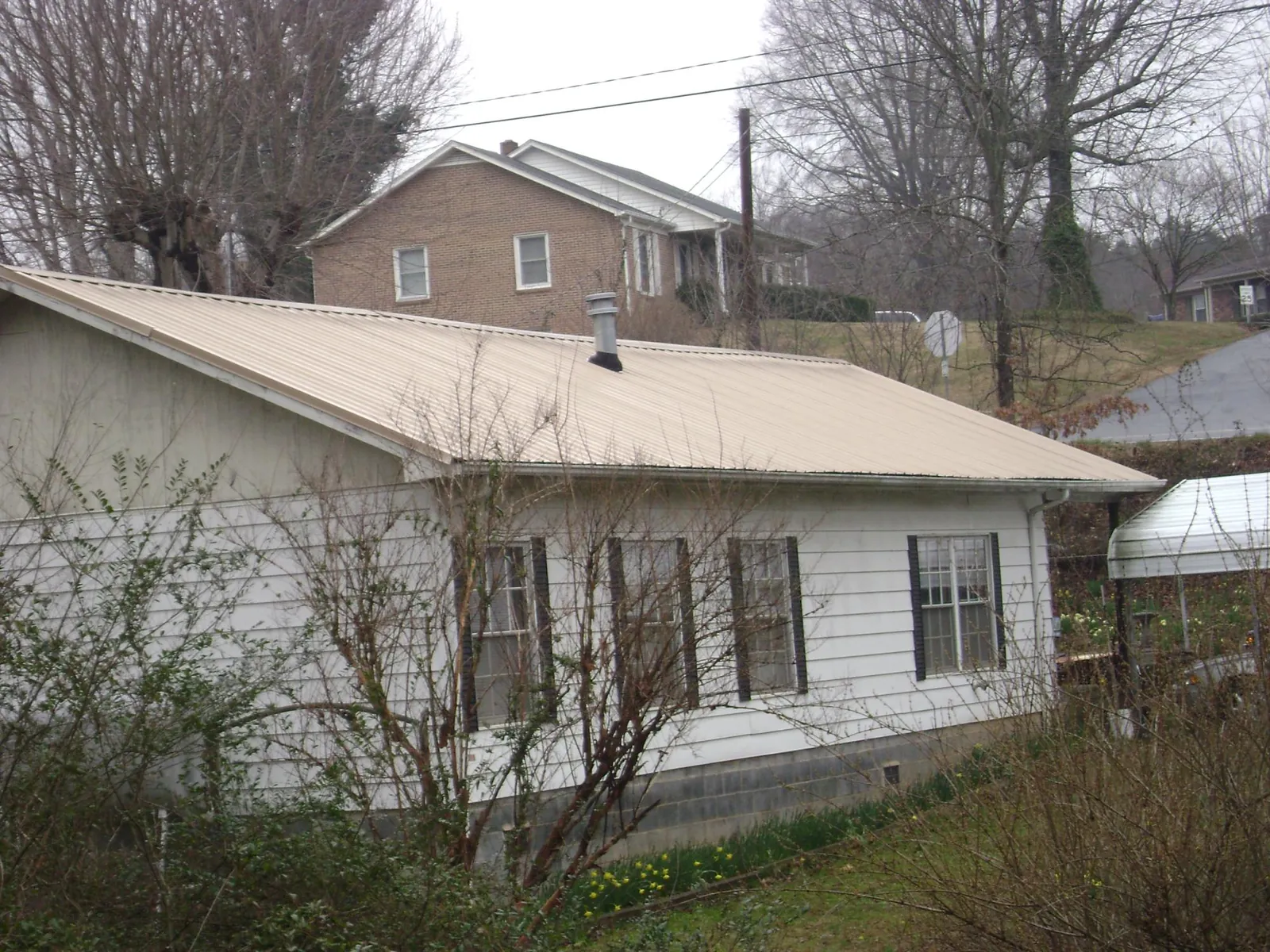 Tan metal roof on a white sided house set into a hillside — Commercial Roofing by Roofing Brothers in Fort Rock